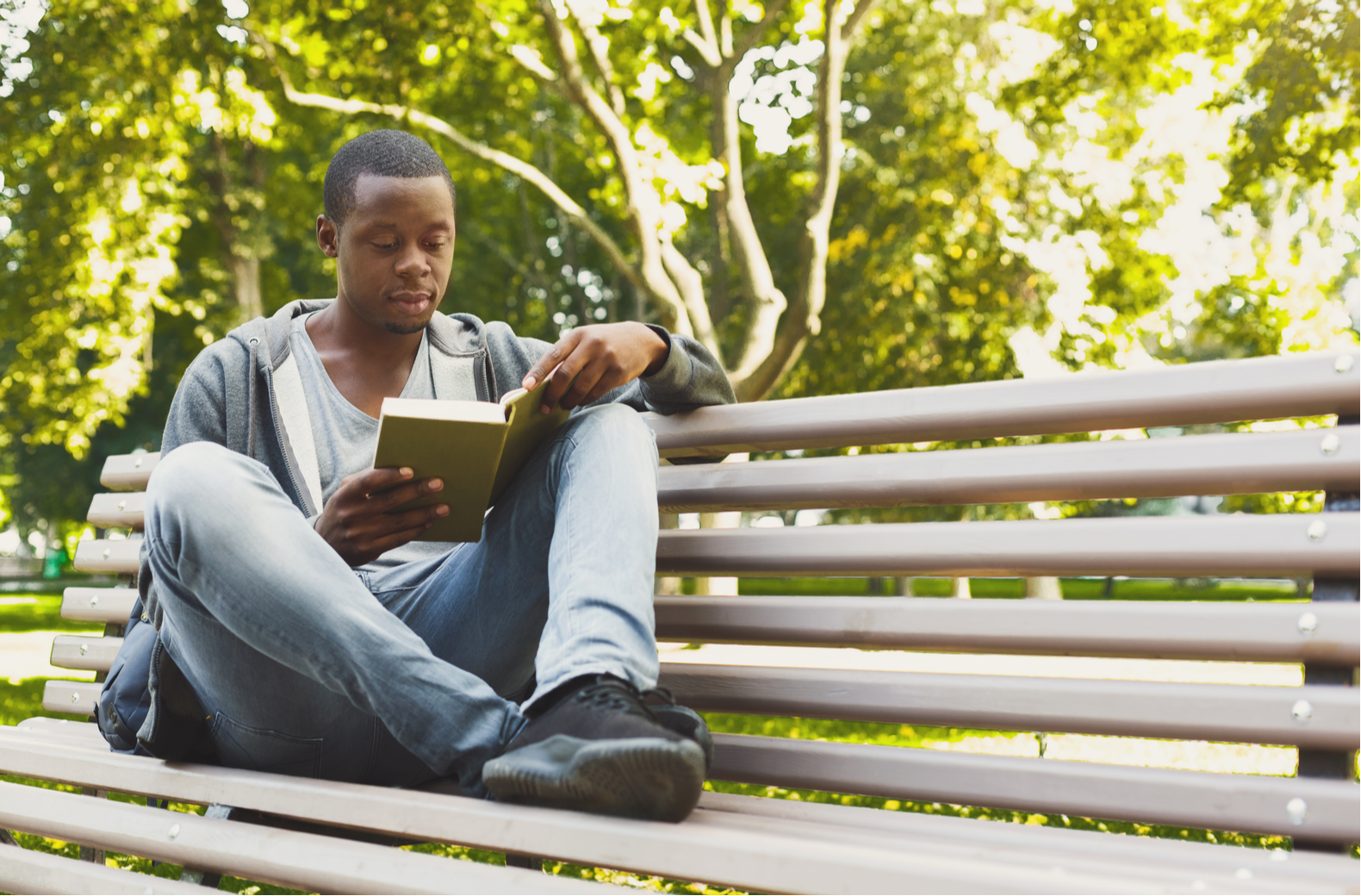 Black man reading on park bench. May is Get Caught Reading Month.