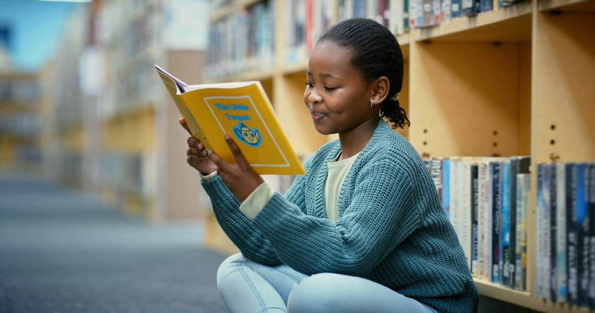 Girl, reading and library with book, story and youth education at school with smile. Development, growth and black child with learning, story and language information with happy student on floor