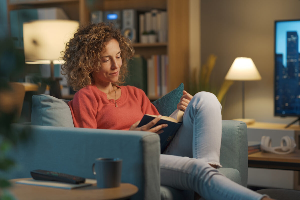 Relaxed happy woman resting on the armchair at home in the living room and reading a book