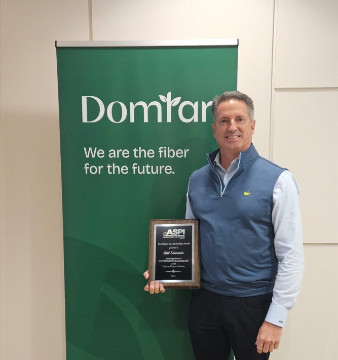 Bill Edwards, Domtar’s senior vice president of paper and packaging operations, holding the ASPI Excellence in Leadership Award in front of a dark green banner with the words in white: “Domtar, “We are the Fiber for the Future.”