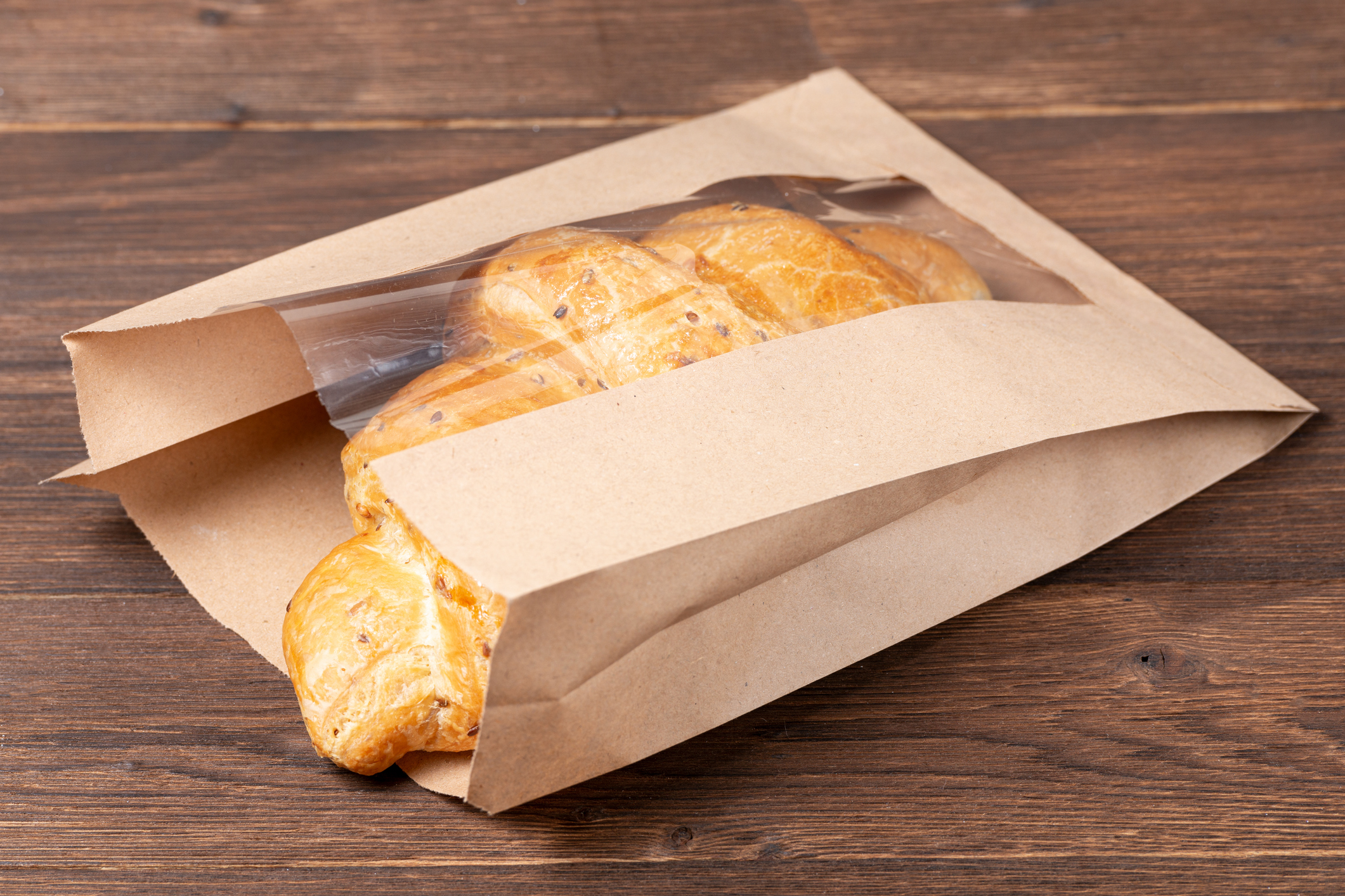 croissant in paper bag on wooden background. concept of continental breakfast and eco packaging, recycling of raw materials