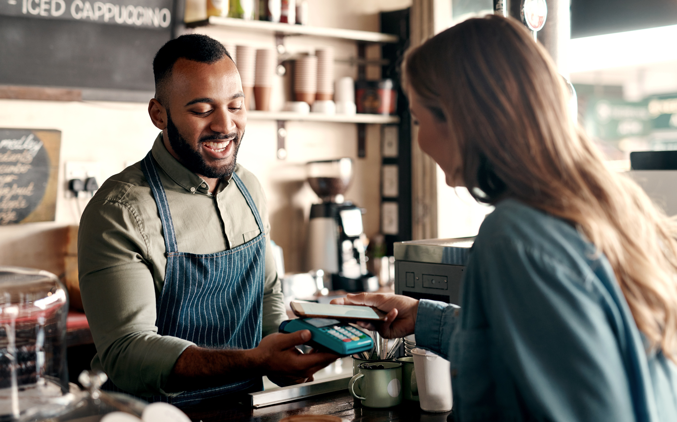 Shot of a young man accepting a digital payment from a customer in a cafe