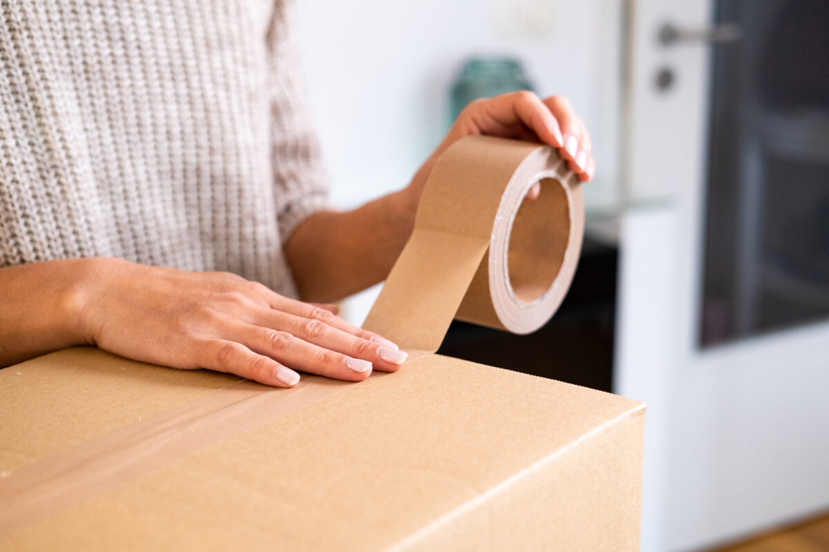 Side view on a woman taping cardboard box in the kitchen.