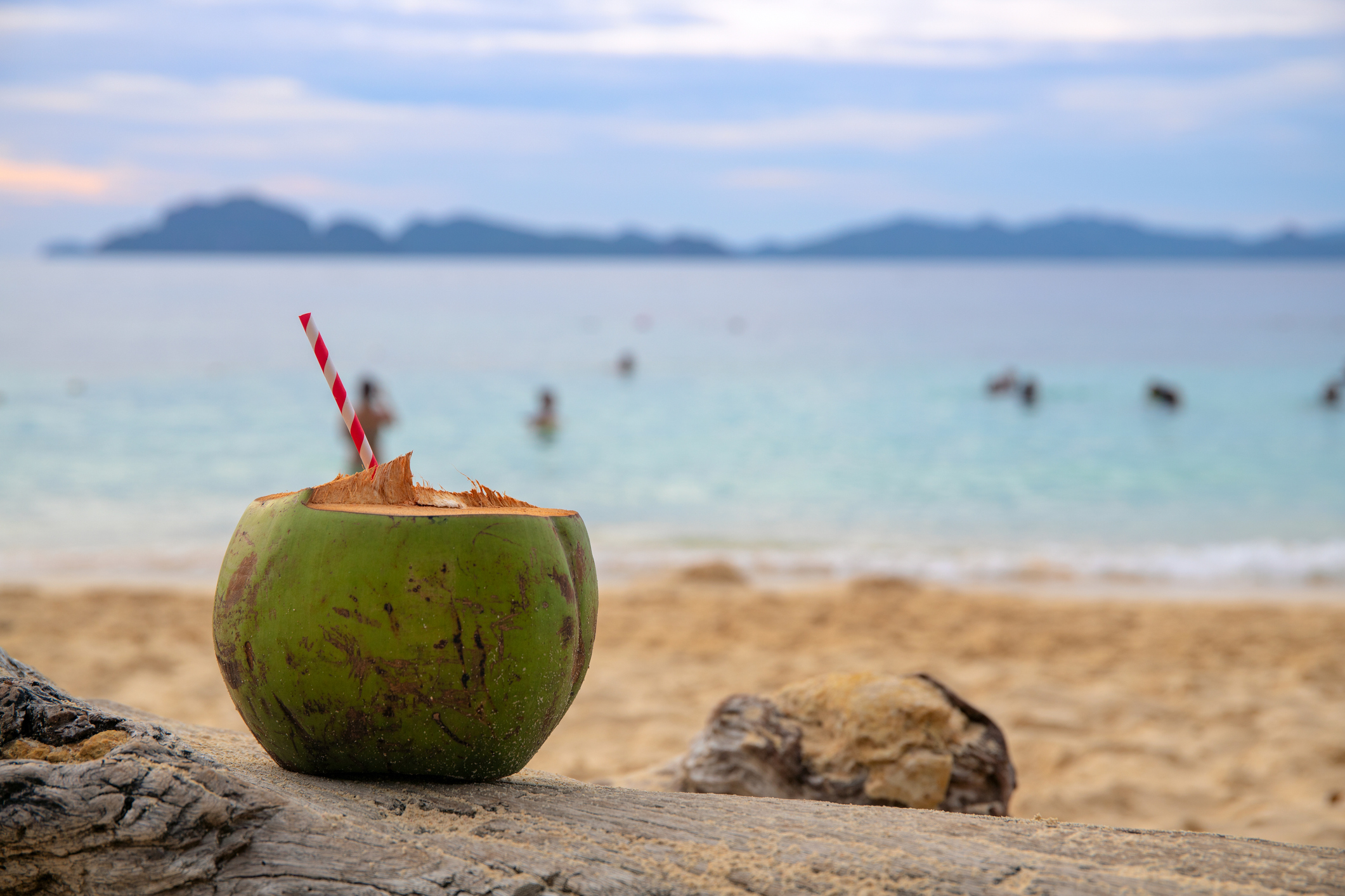 Green coconut drink with straw on sea beach sand. Coconut juice on tropical seashore. White sand beach relax. Green coconut cocktail with paper straw. Exotic vacation on Philippine island beach