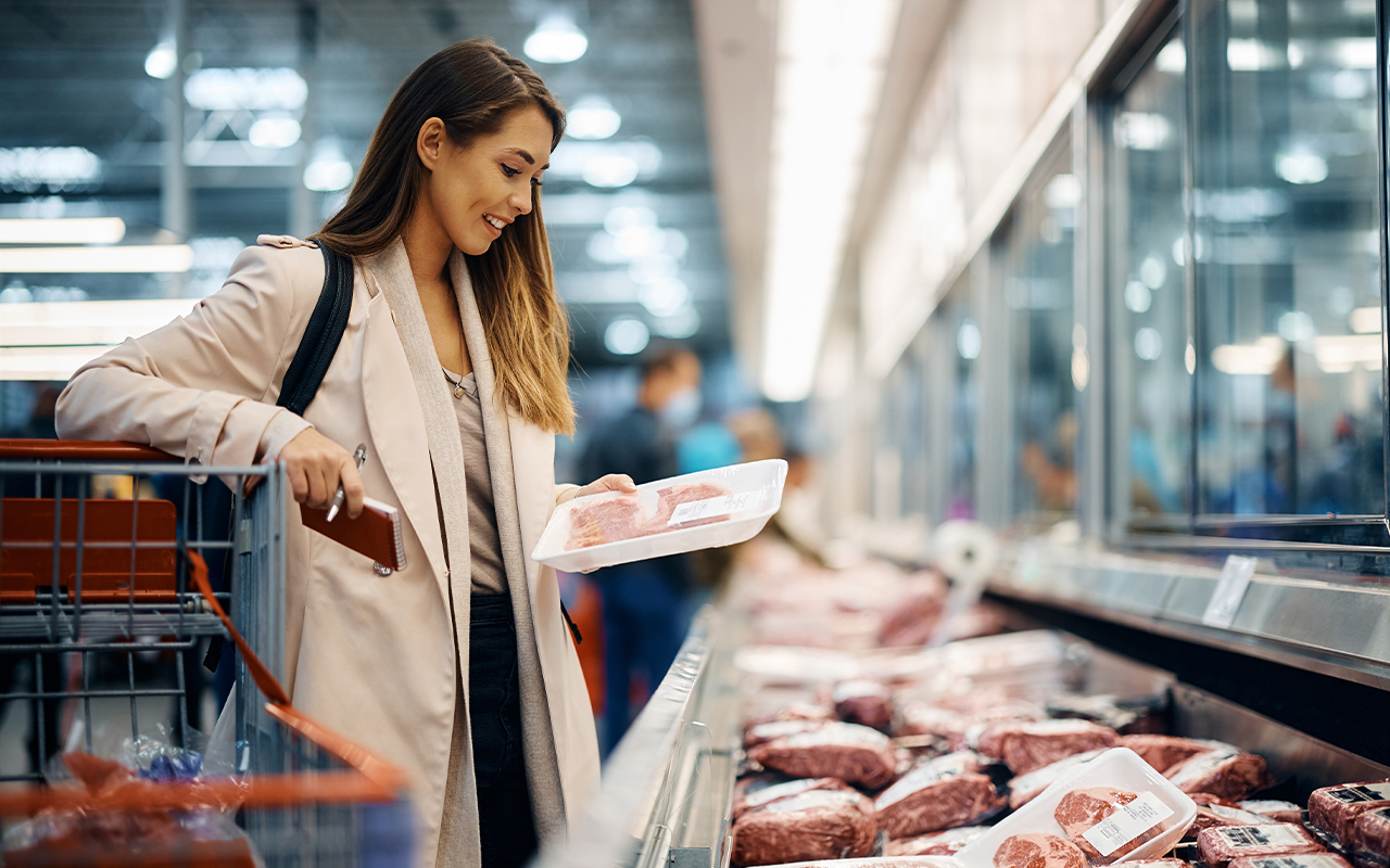 Young happy woman choosing fresh meat while buying food at the supermarket.