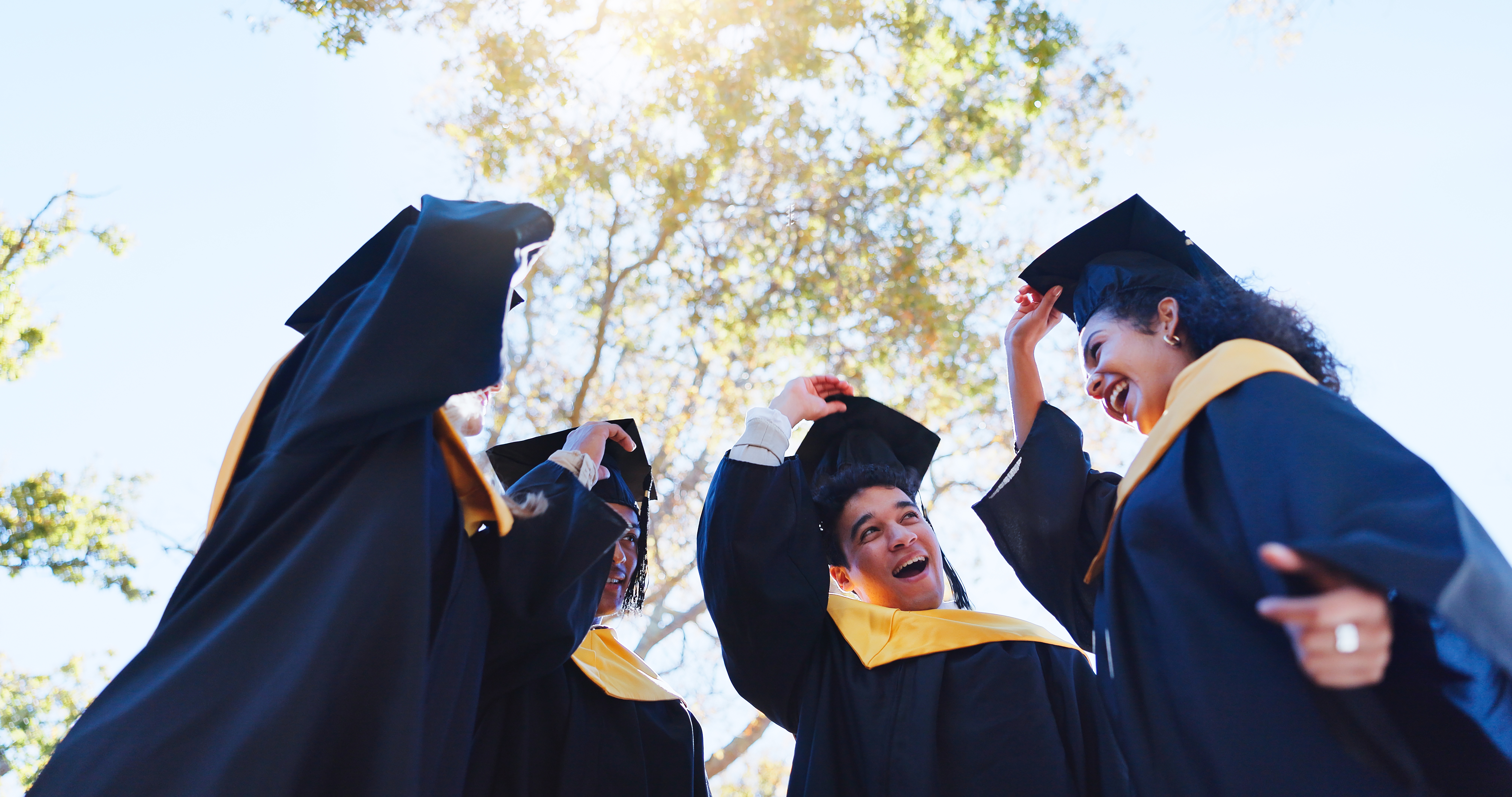 three graduating student removing their caps to toss them into the sky